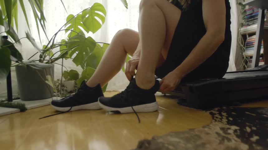 A female person is putting black sneakers on her feet