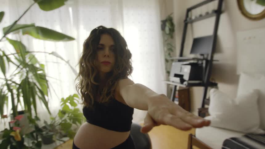 A pregnant woman is doing a yoga pose in her living room