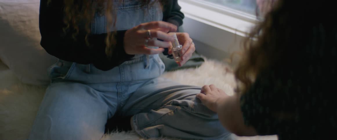 One woman paints friends fingernails as they sit on bed near window