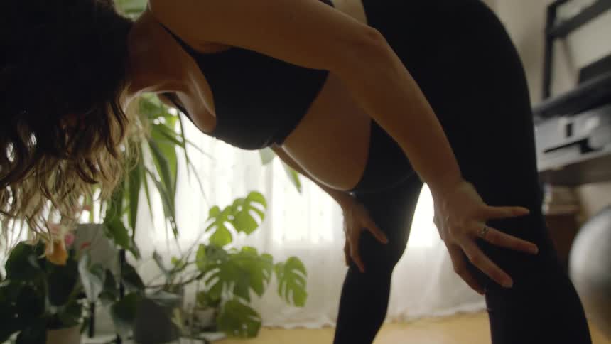 Woman with wavy hair black sports bra and leggings exercises on black fitness mat in the living room at home