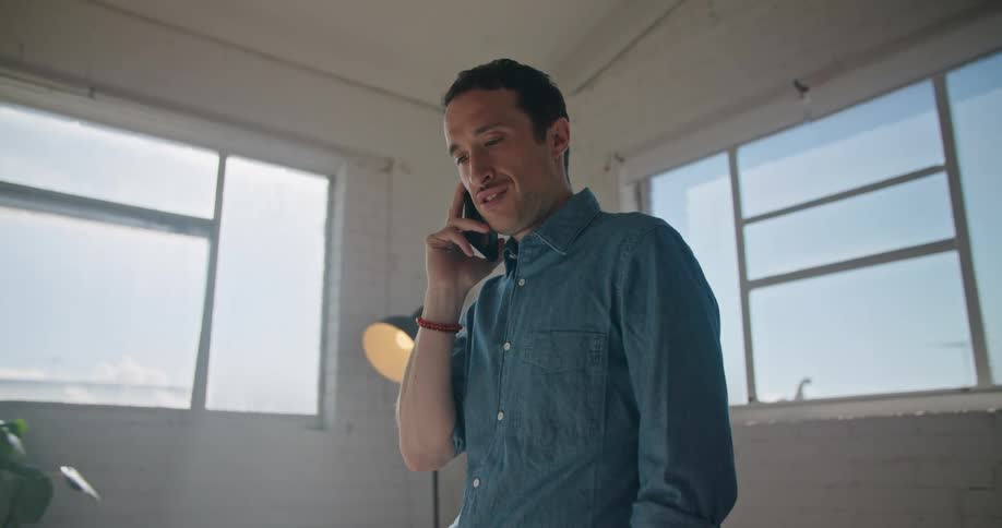 Man stands in office near windows talking on mobile phone