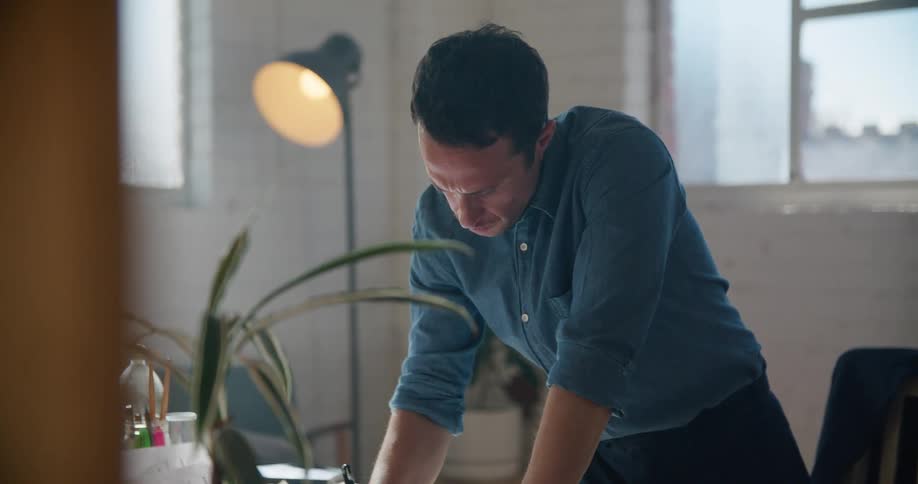 A man uses a pen to write on a blueprint while standing before a desk in an office during the day