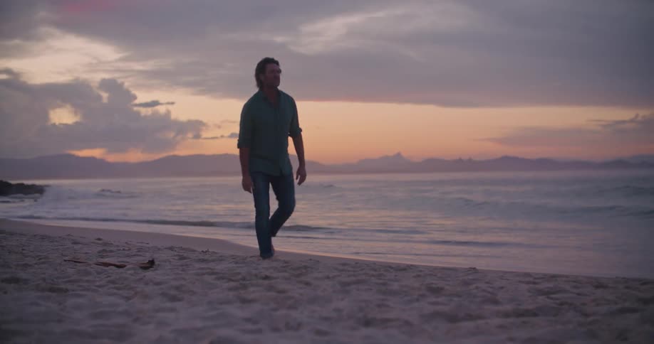 A man walking on a beach with the ocean sky and clouds in the background