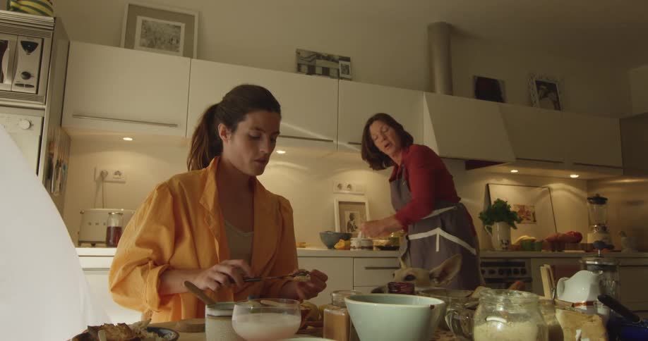 Two women work on meal together as curious dog looks on