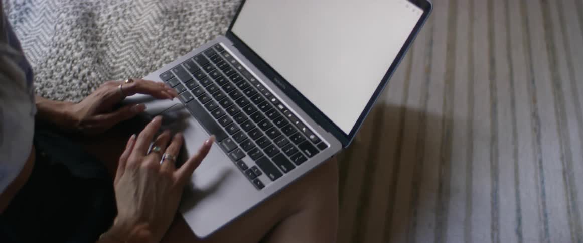 A woman with several rings on her manicured hands types on a computer in her lap as she works from the comfort of home.