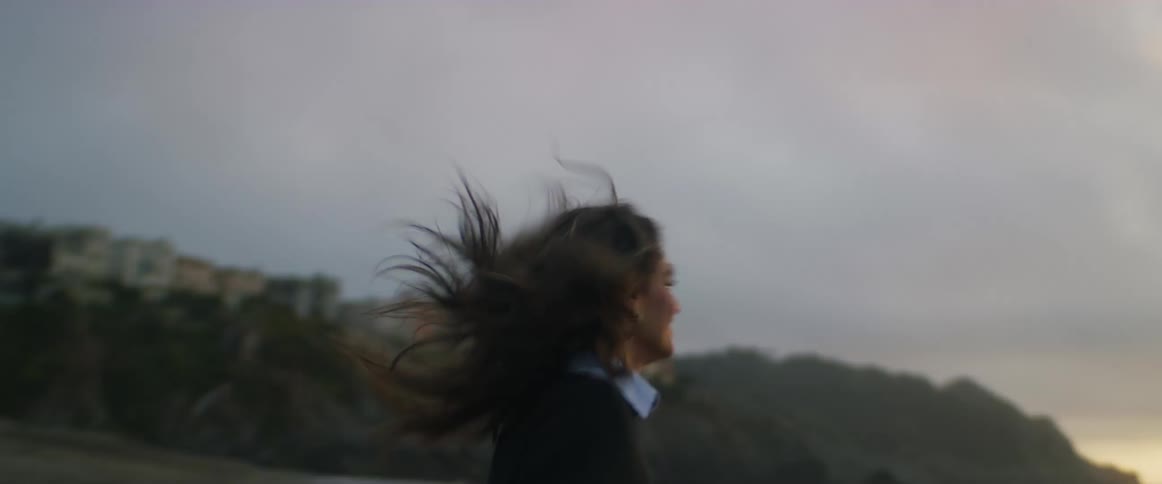 A woman laughs and spins around as she runs toward the ocean