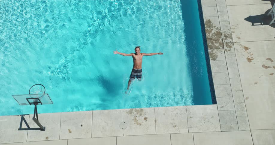 A man is smiling while falling back and splashing into a swimming pool