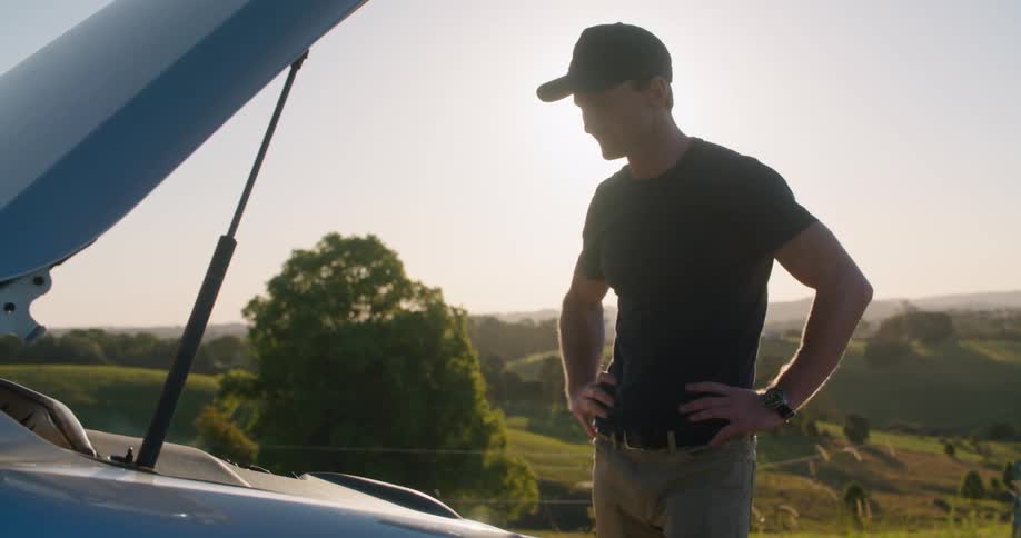A man looking at an engine in a car that is smoking
