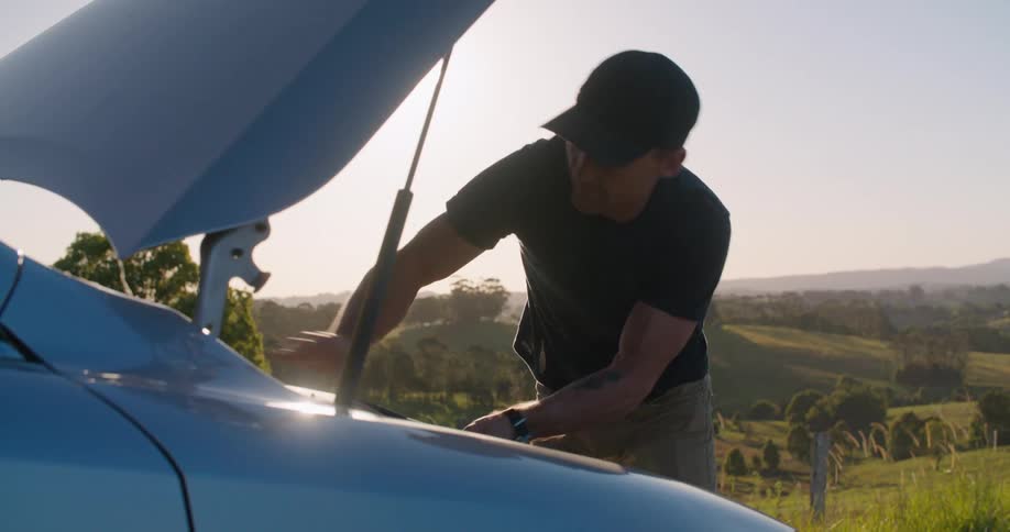 A man opens the trunk of a car and is looking inside as the sun shines brightly behind him