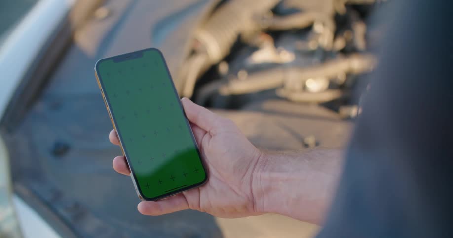 Man stands near car with front hood up scrolling on his phone