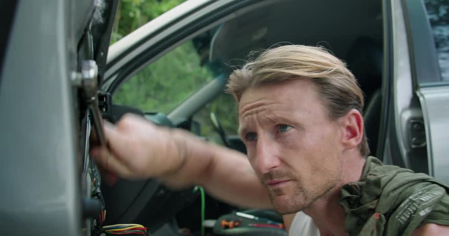 A man using a tool on a vehicle door with trees and leaves in the background