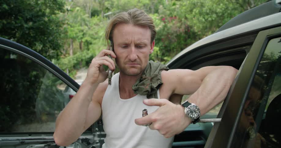 A man with a smart phone and a tool sitting in an open vehicle with trees in the background