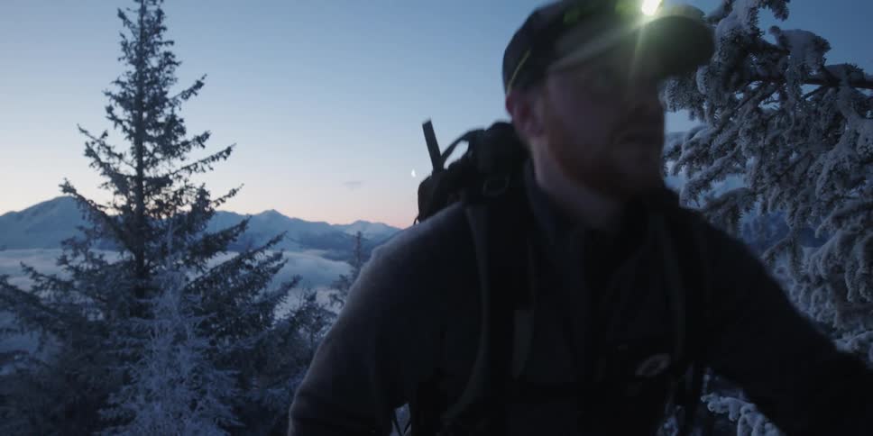 A man wearing a headlight is hiking up a mountain in the snowy wilderness