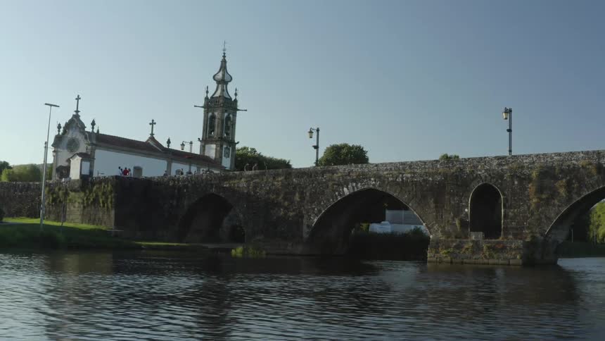 People stand on stone bridge spanning river near church