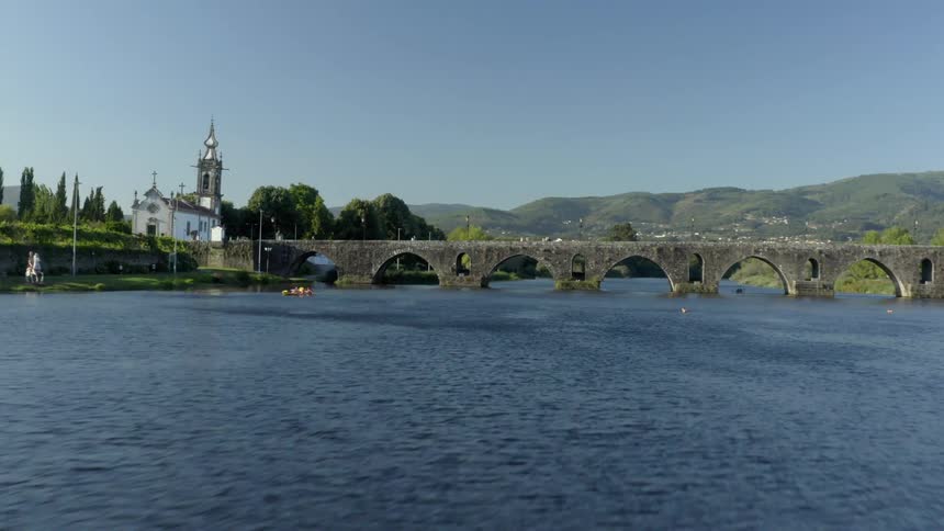 An aerial view of a waterway with a walking bridge in a small rural town with mountains in the background in the daytime