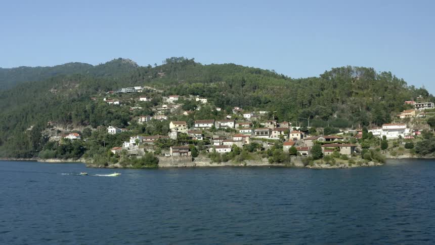 Aerial view of boats passing by coastal town with mountains in the background
