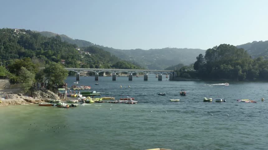 Many people are on a beach and on floats and boats in a river