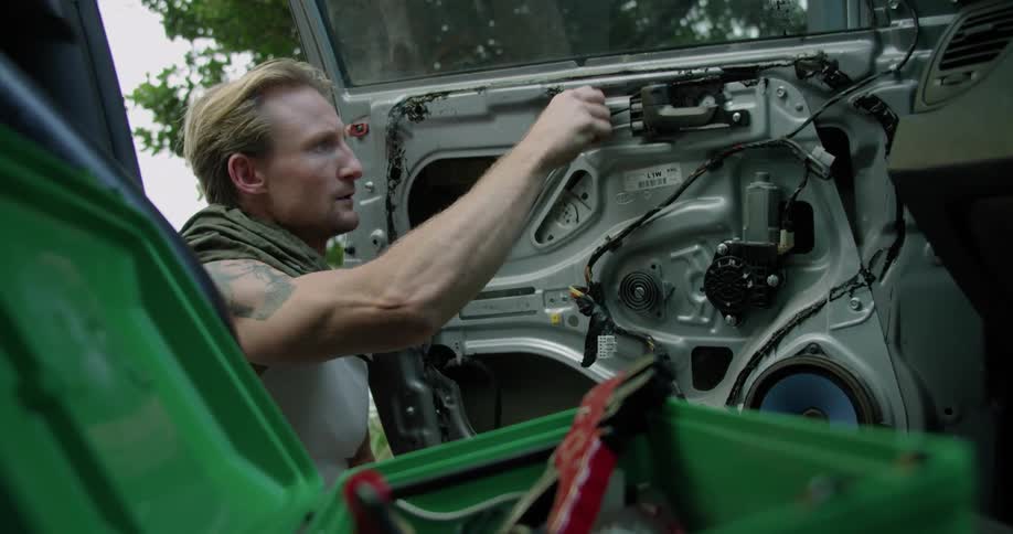 A man using a tool on a vehicle door with trees the sky and clouds in the background