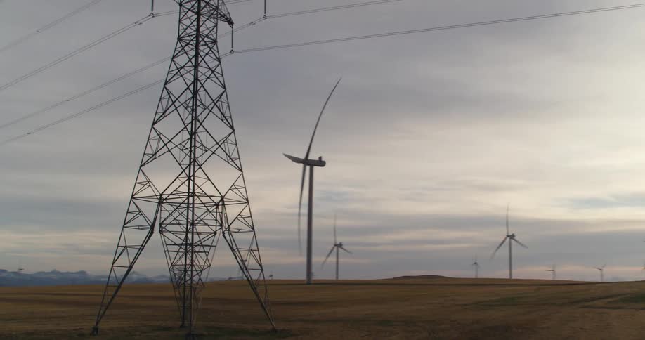 Passing by a large windmill farm on farmland with snowcapped mountains in the distance on an overcast evening