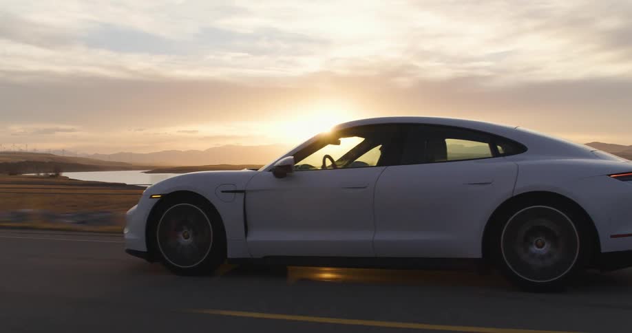 White electric sports car driving on a rural road near a river in the plains at sunset