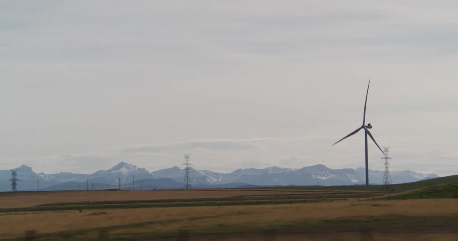 Passing by a large windmill in a large field with a mountain range in the distance on a cloudy day