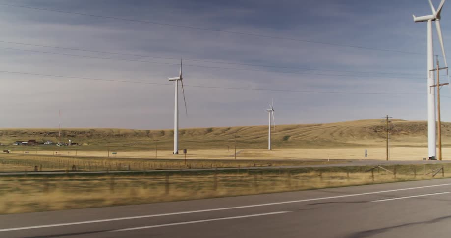 Passing by a wind farm with large windmills on farmland during the daytime