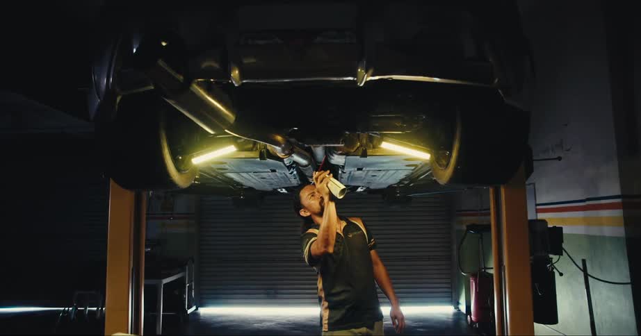 Man spraying the underside of a car raised on a lift inside a shop
