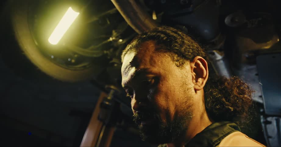 A mechanic stands under a vehicle lifted up in a garage