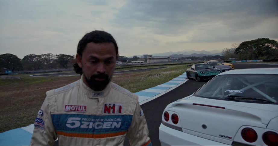 A race car driver holds his helmet while walking away from the track