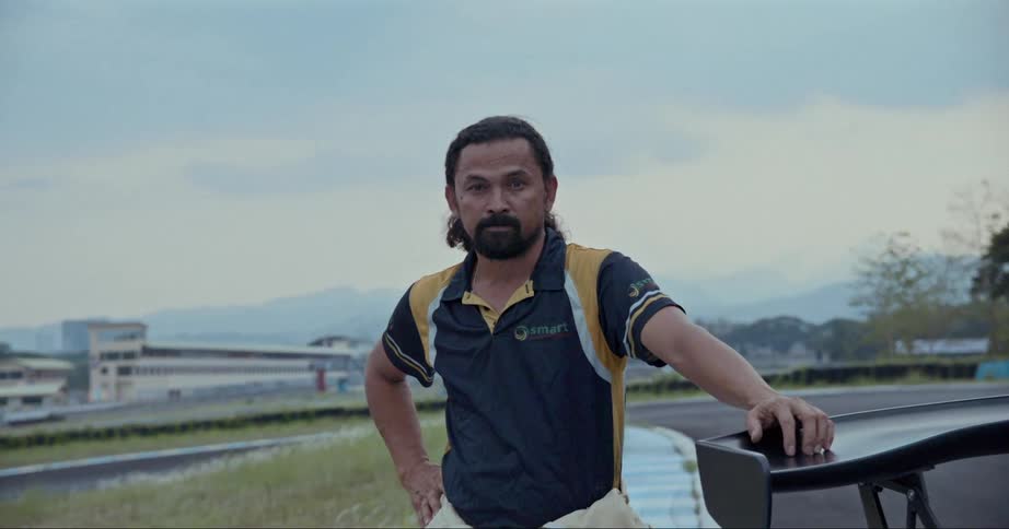 Portrait of a man standing next to a sports car with mountains in the background during the day