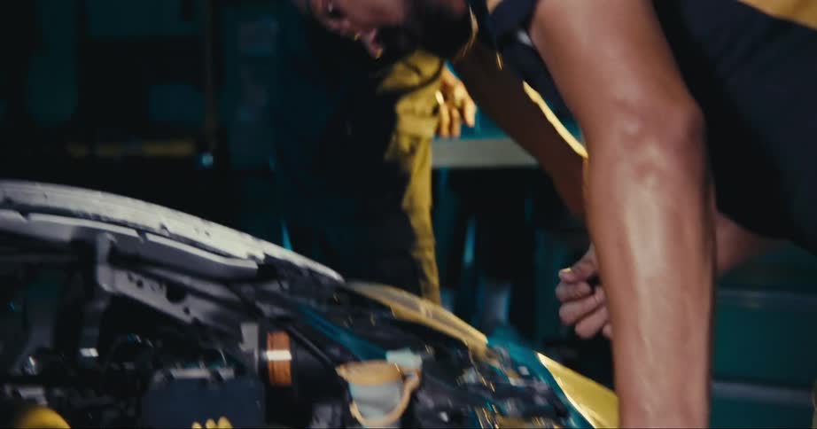 Two mechanics work on car engine in garage