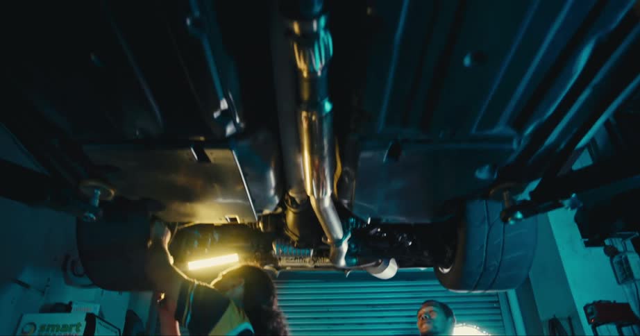 Two men with matching jerseys in a garage working on a vehicle with a wall in the background