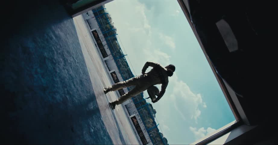 A race car driver stands in a garage doorway with hands on hips holding his helmet