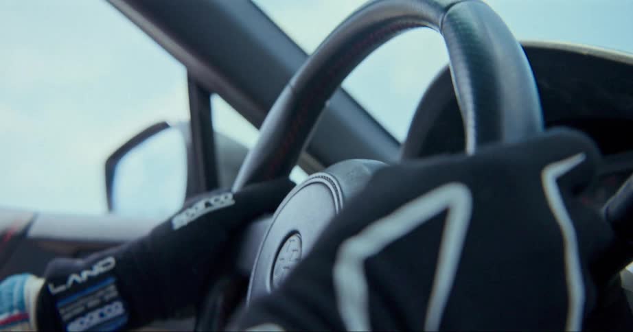 A person with gloves in a vehicle turning the steering wheel with the sky and clouds in the background