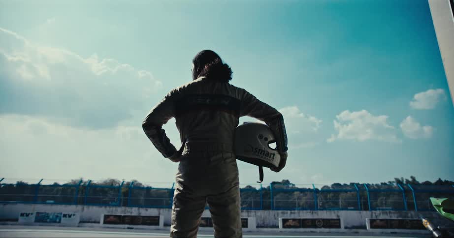 A racecar driver stands holding his helmet while standing in a garage doorway at a racetrack facility