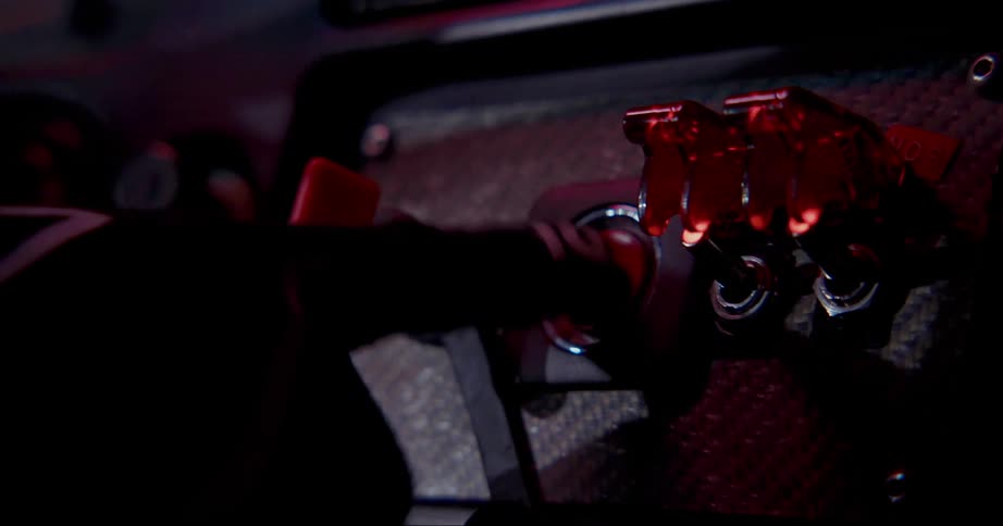 Hand in a glove pressing buttons and switches on the dashboard of a race car at night