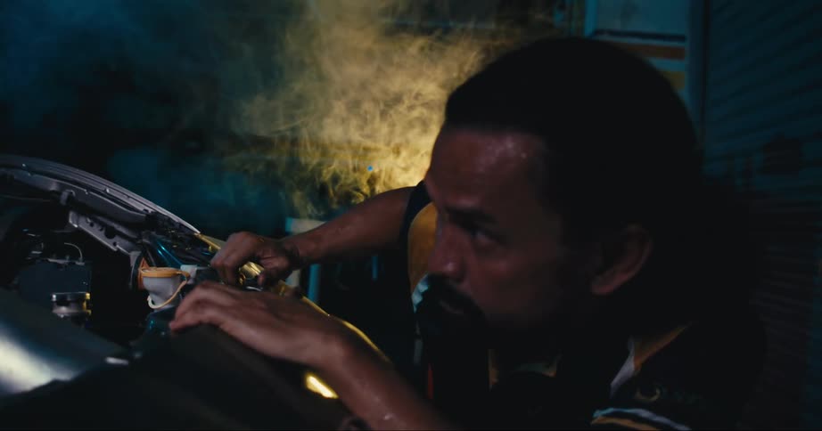 A man is crouching by a car engine