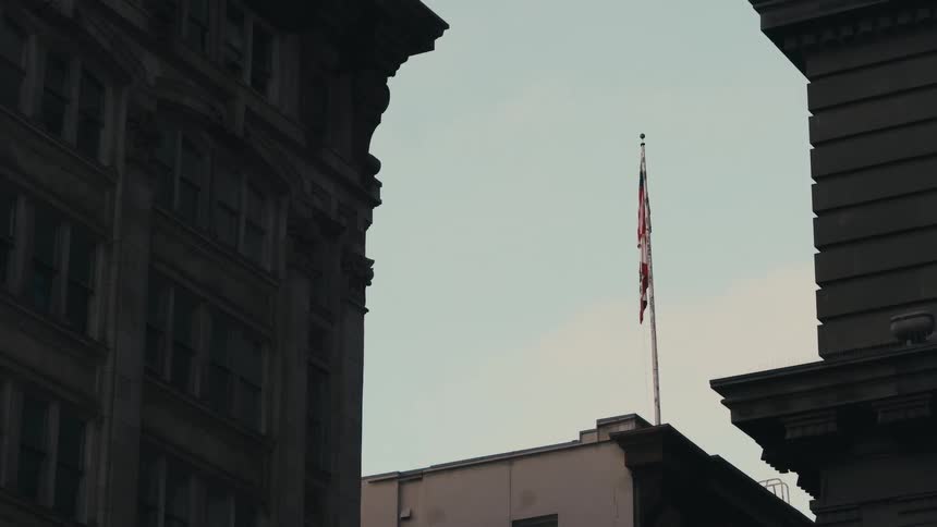 Flag hangs loosely on flagpole on roof of building showing between two architecturally detailed buildings