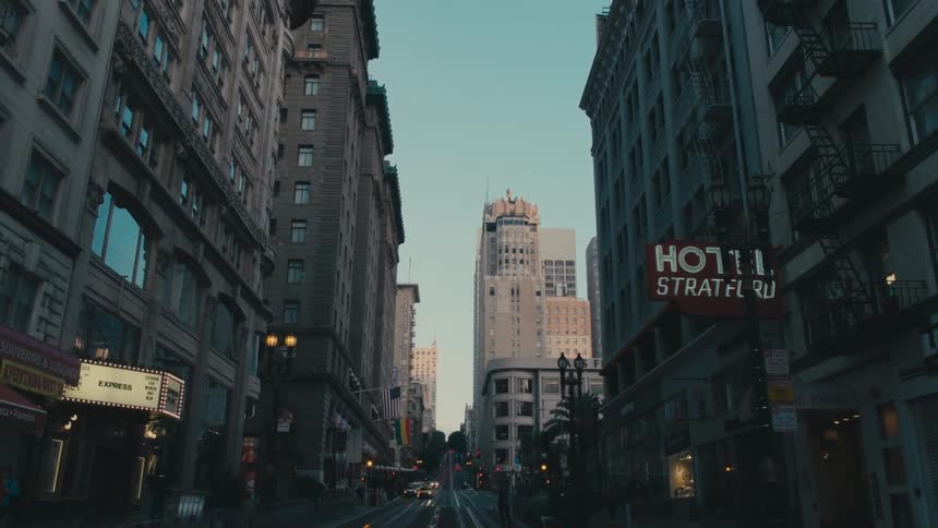 A city street with vehicles and people with the sky and clouds in the background