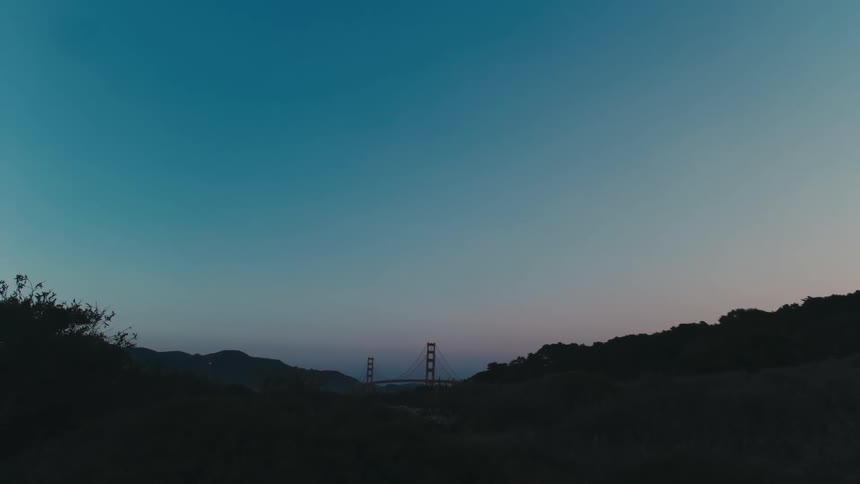 Slopes lead to suspension bridge on horizon under lightly tinted pink sky