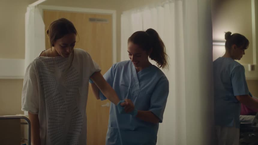 A woman helping another woman walk in a hospital
