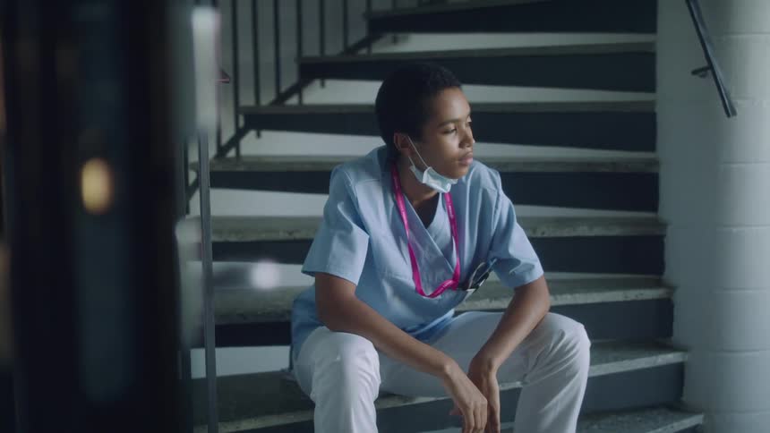 Nurse sits on bottom of staircases staring before taking deep breath