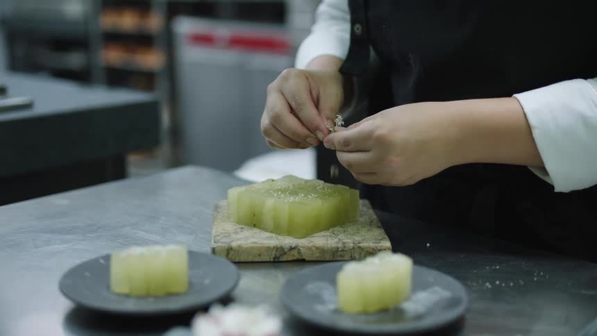 A chef adds garnish to plated food on a stainless counter