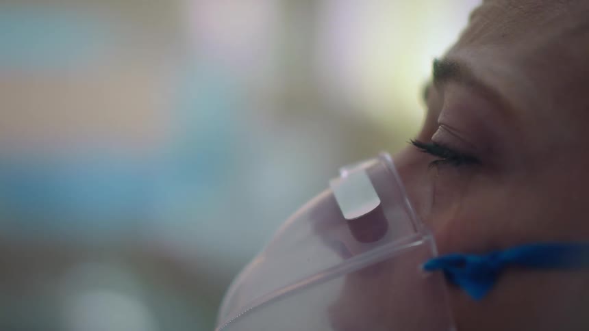 Sad woman wearing an oxygen mask while laying in a hospital bed crying