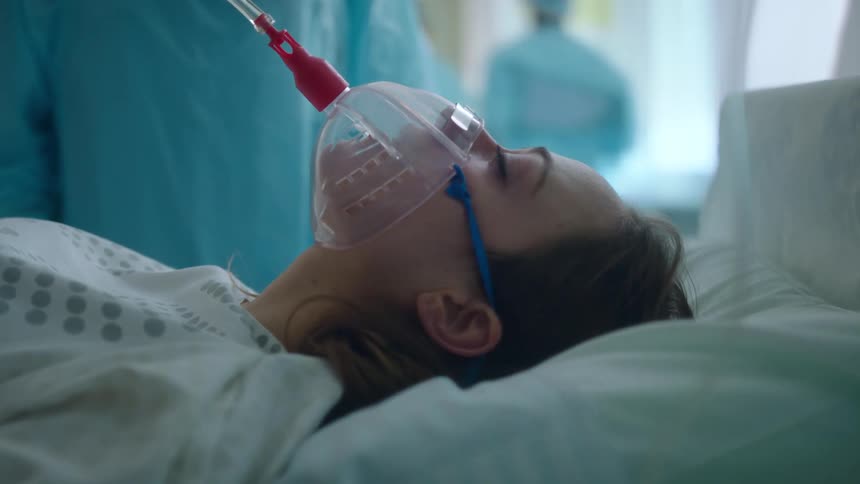 Doctors wearing protective clothing puts oxygen mask on woman in operating room