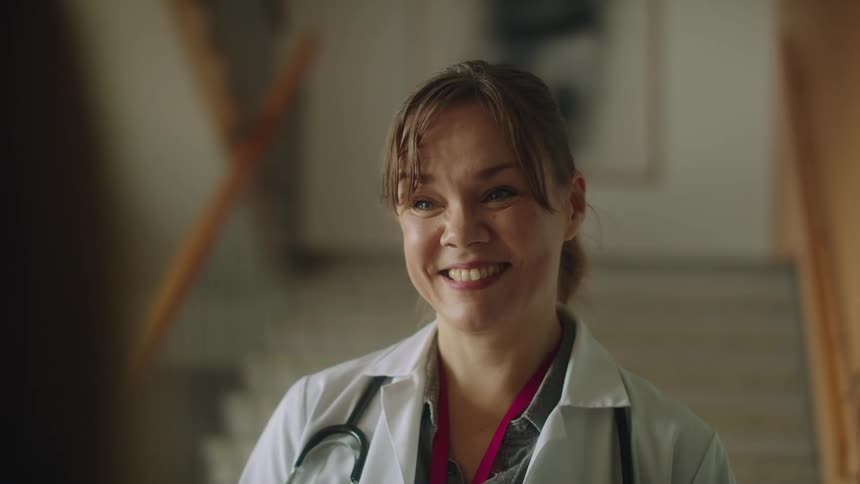 Middle aged doctor with white lab coat and stethoscope talks to patient smiling in the hospital