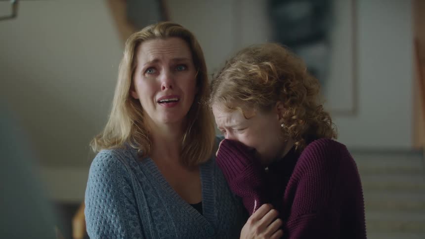 Two women in a room hugging and crying with a wall in the background