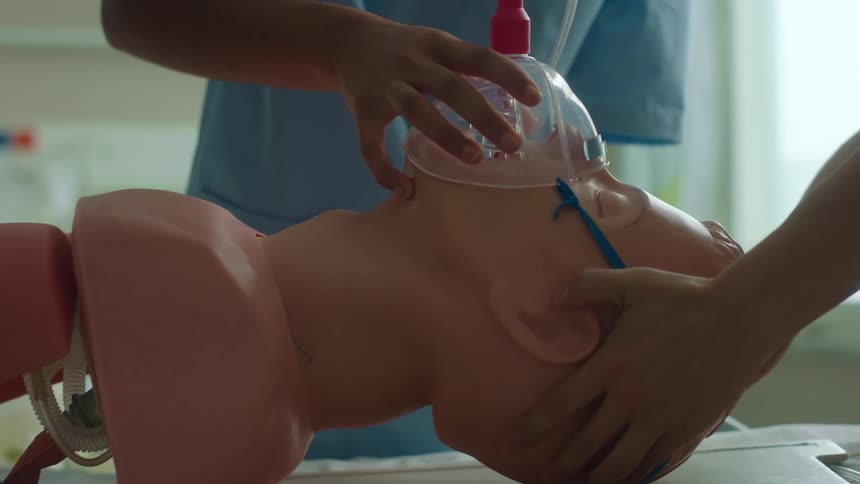 Nurses with blue scrubs put oxygen mask on manikin