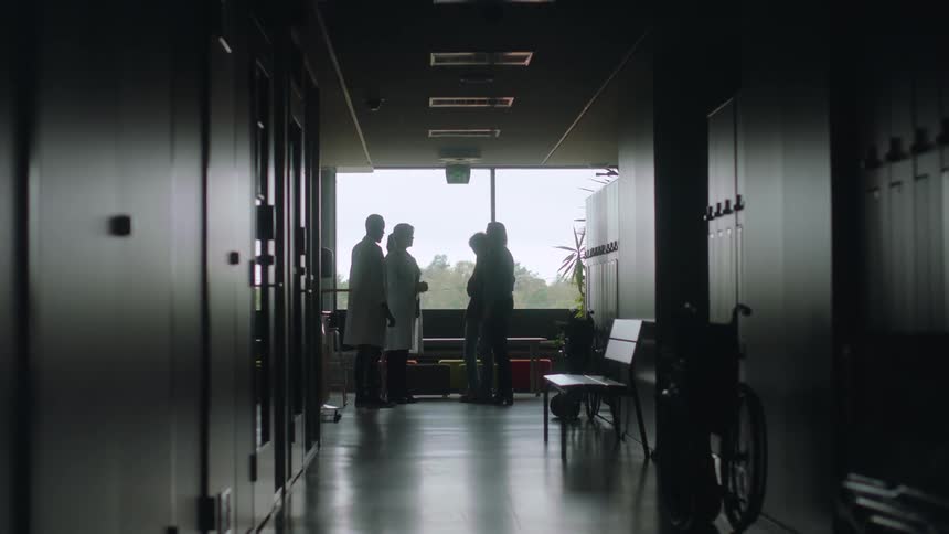Two doctors at the end of a hospital hallway talking to two women