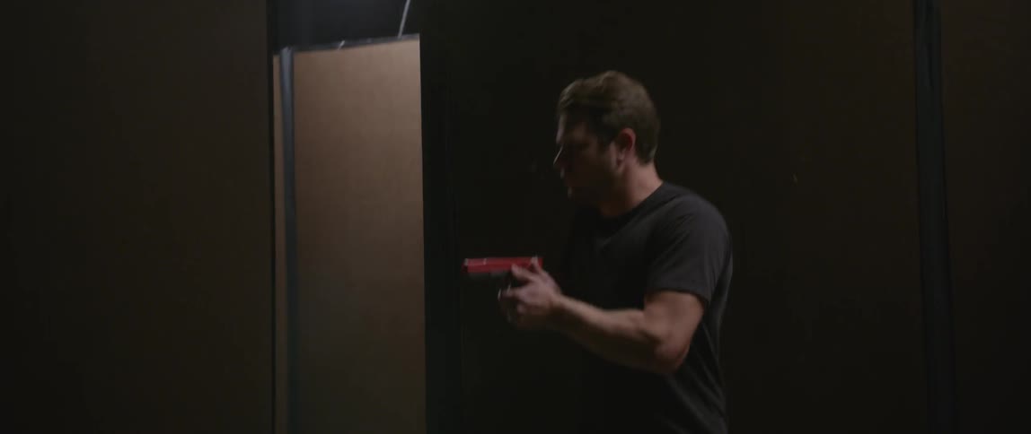 A man holding a gun looks around a wall